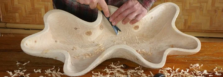 Person schnitzt Schale aus Holz mit Werkzeug